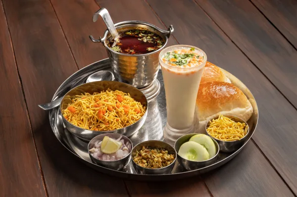 Bowl of misal with sprouted beans in red spicy gravy, topped with farsan, onion and coriander, served with buttered pav
