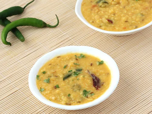 Bowl of golden moong daal topped with garlic tarka, red chillies and fresh coriander, served with rice and roti