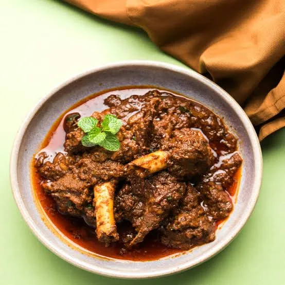 A copper pot of mutton korma with thick golden-brown gravy, garnished with ginger and coriander, served with naan