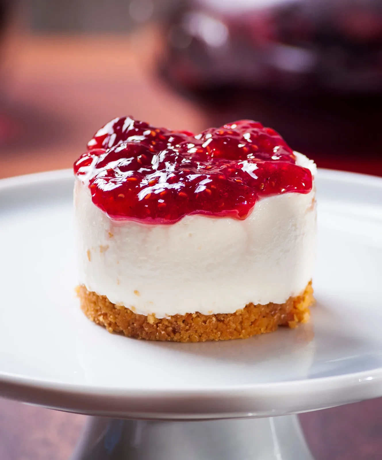 Slice of no-bake cheesecake with a biscuit base and fresh strawberry topping on a white plate