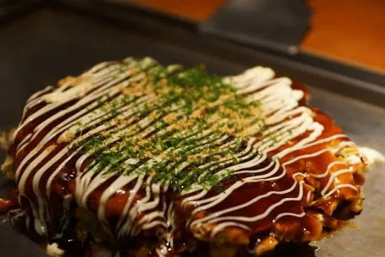 Okonomiyaki cabbage pancake topped with sauce, mayonnaise and nori, with one wedge cut out
