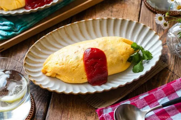 Soft yellow omelette over ketchup chicken rice, drizzled with ketchup and garnished with parsley