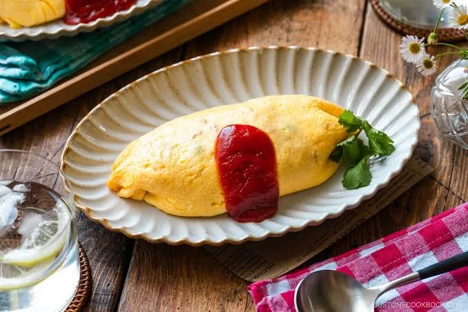 Soft yellow omelette over ketchup chicken rice, drizzled with ketchup and garnished with parsley