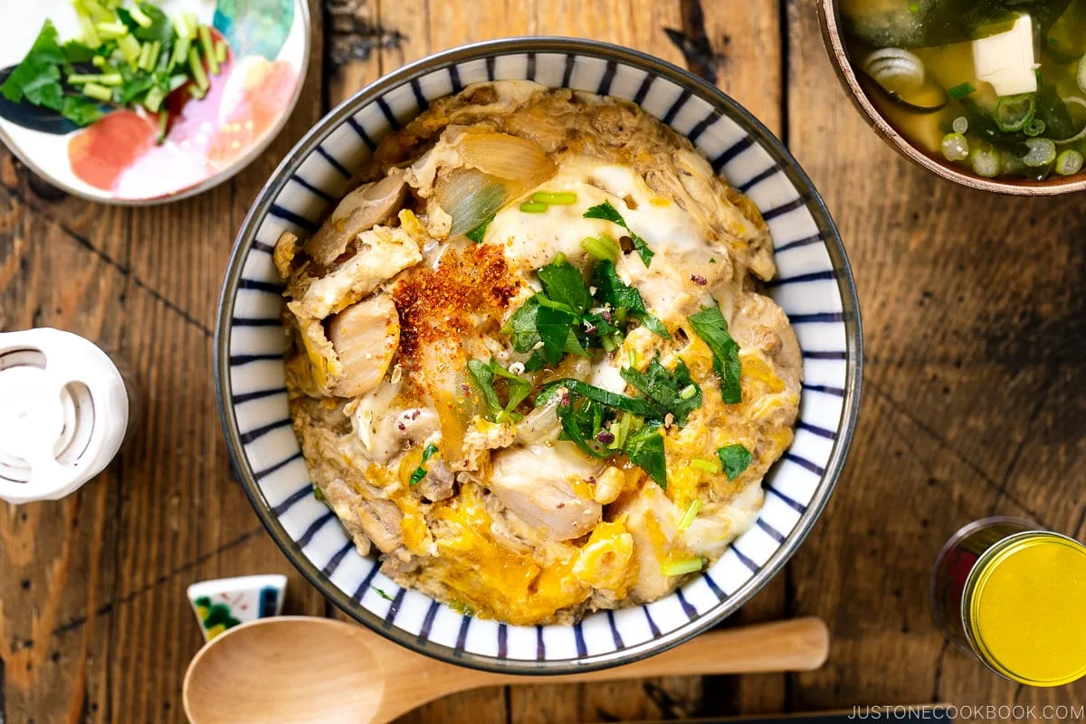 A bowl of oyakodon with soft egg and chicken over rice, topped with spring onion
