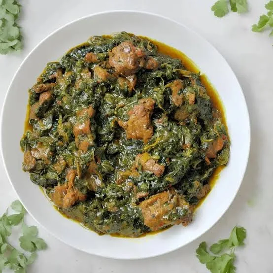 A pot of dark green Palak Gosht with pieces of mutton, topped with ginger matchsticks, served with roti and lemon wedges