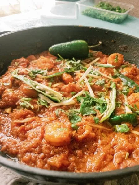 A pan of prawn masala with pink prawns in a thick tomato gravy, garnished with fresh coriander, served with rice and roti