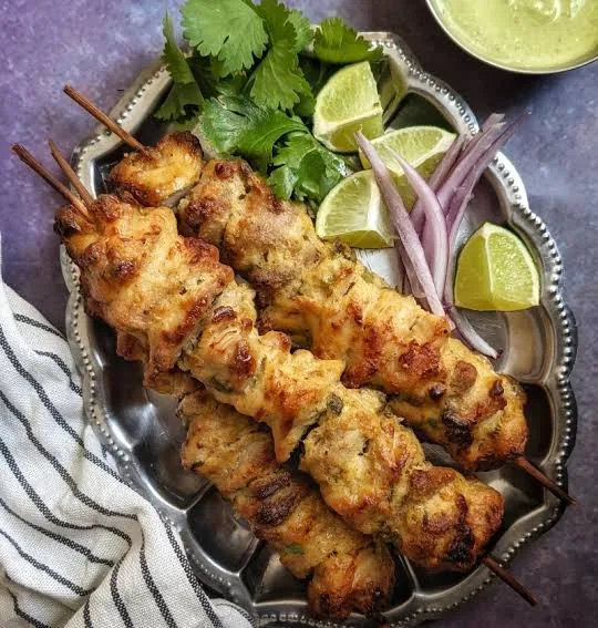 Golden grilled reshmi chicken kababs on skewers with mint chutney, onion rings, lemon and naan
