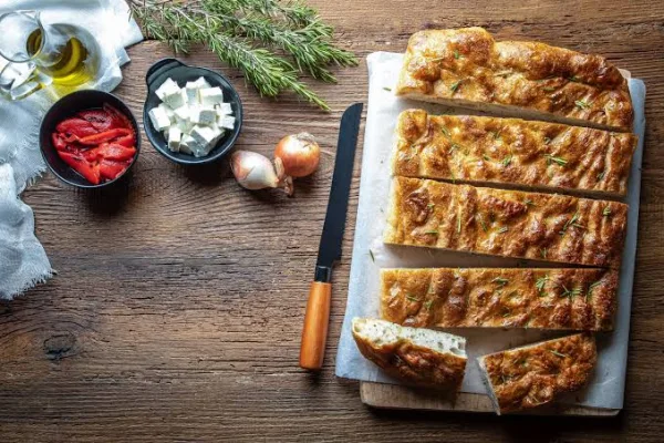 Golden rosemary focaccia in a baking tray with olive oil dimples, rosemary sprigs and coarse salt on top