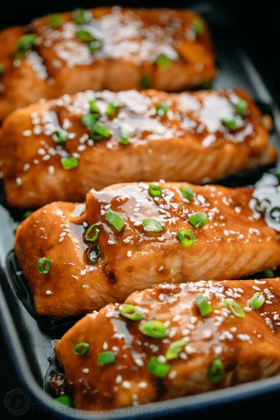 Glazed teriyaki salmon fillet over steamed rice with broccoli, sesame seeds and spring onions