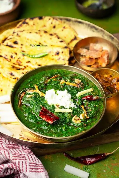 A bowl of thick green sarson ka saag topped with white butter and a ghee tarka, served with makki ki roti