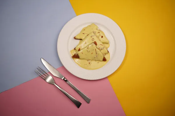 Golden fried bread triangles topped with thick saffron milk and sliced pistachios in a white dish