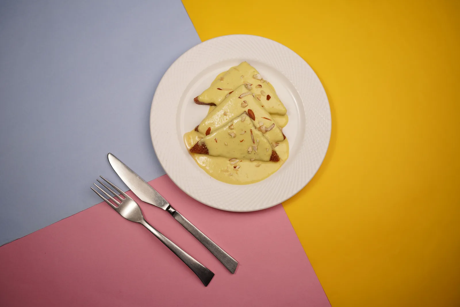 Golden fried bread triangles topped with thick saffron milk and sliced pistachios in a white dish