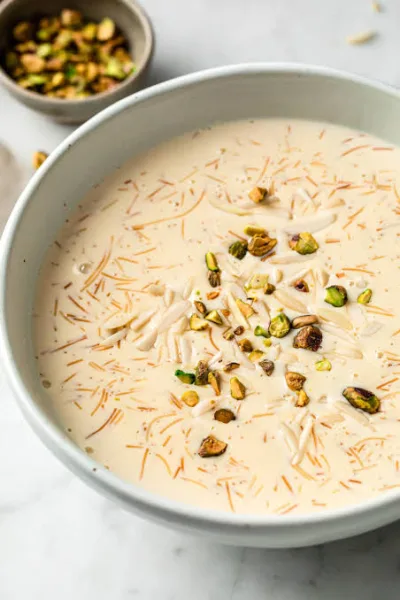 Bowl of sheer khurma with vermicelli, dates and sliced nuts, garnished with pistachios and saffron