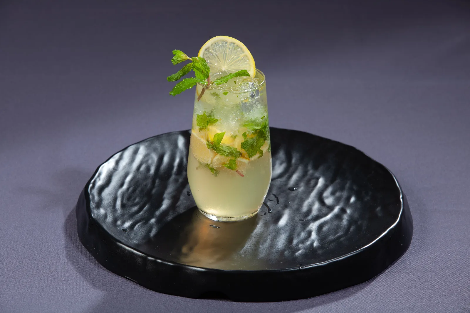 Tall glasses of iced shikanjvi with lemon slices and mint, beside halved lemons and a jug of the drink