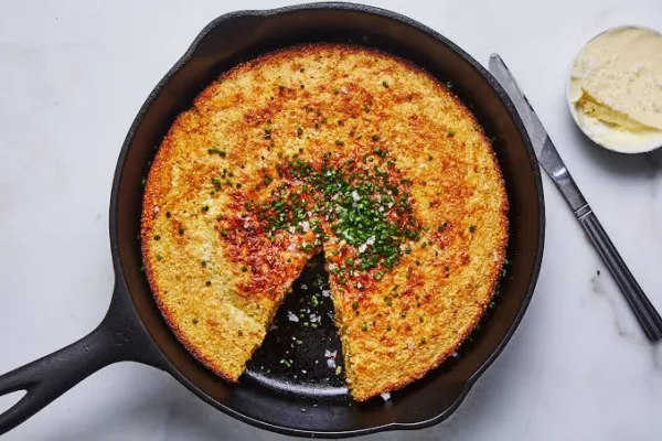 Golden skillet cornbread in a cast iron pan with one wedge cut and a pat of melting butter on top