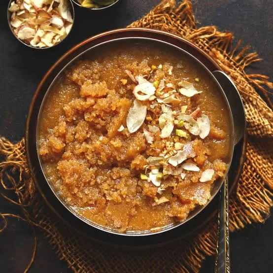 Golden semolina halwa garnished with almonds and pistachios in a small brass pan