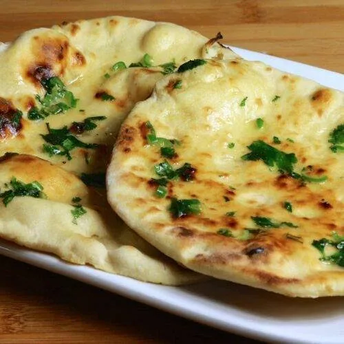 Stack of freshly cooked butter-brushed naan topped with nigella and sesame seeds on a wooden board