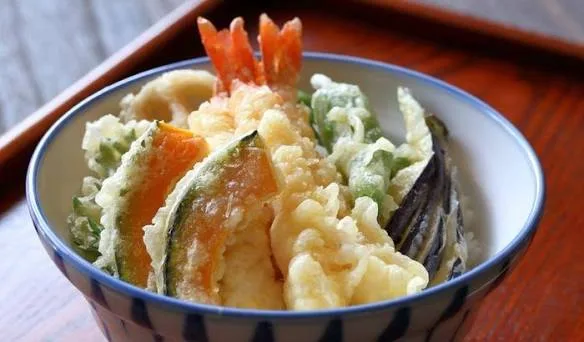 Bowl of rice topped with golden prawn and vegetable tempura glazed with soy sauce and garnished with spring onion