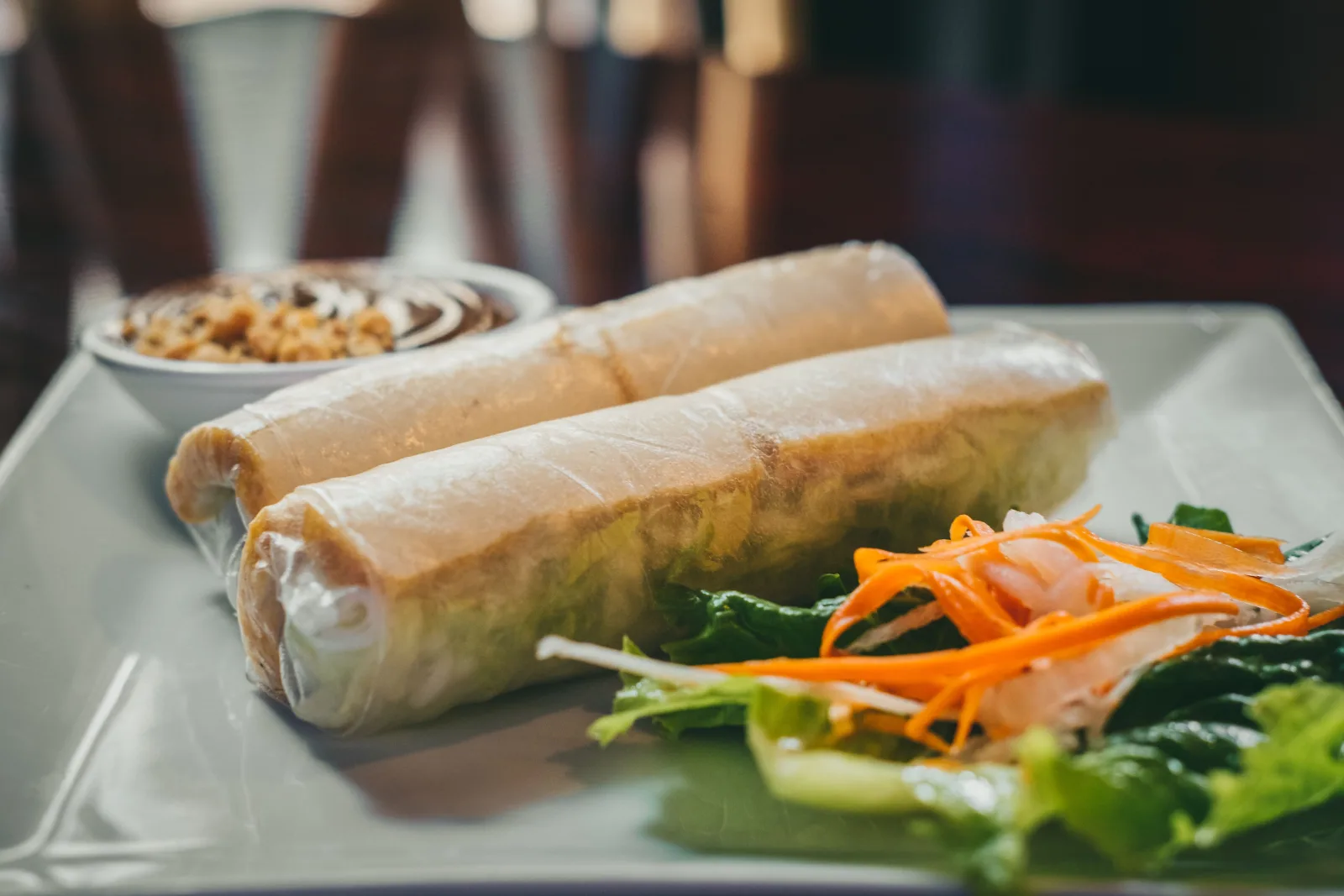 Golden fried vegetable spring rolls on a plate, one cut open to show cabbage and carrot filling, with chilli sauce