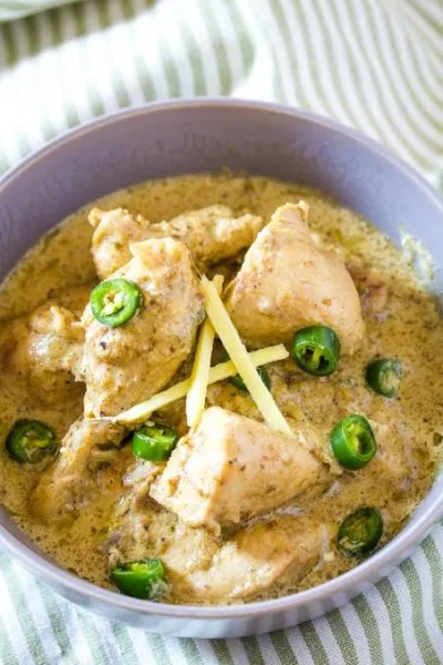 A karahi of creamy white chicken curry garnished with ginger strips, green chillies and fresh coriander, served with naan