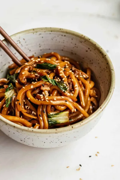 A bowl of yaki udon with chicken, cabbage and carrot, topped with spring onion and sesame seeds
