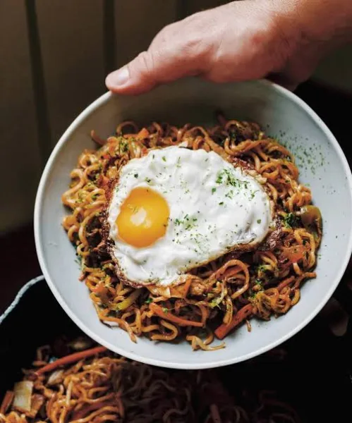 Plate of yakisoba noodles with chicken, cabbage and carrot, garnished with pickled ginger and spring onion