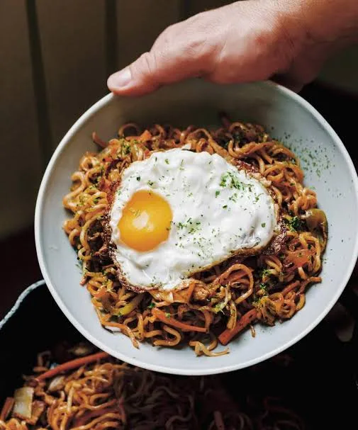 Plate of yakisoba noodles with chicken, cabbage and carrot, garnished with pickled ginger and spring onion