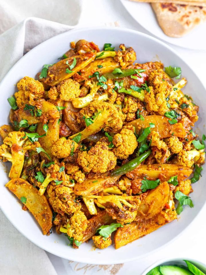 A karahi of dry-style aloo gobi with potato and cauliflower in golden masala, topped with ginger and coriander
