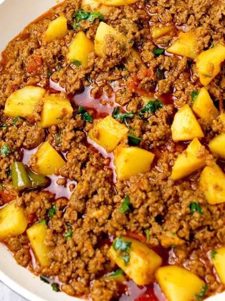 A pot of aloo keema with minced beef and potato cubes in thick masala, topped with coriander and ginger, served with roti and raita