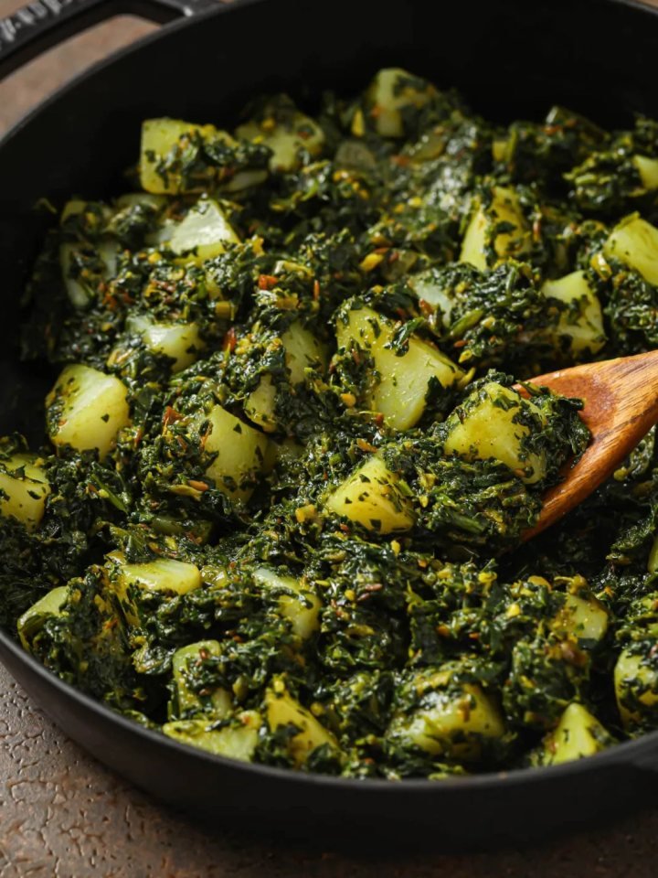 A bowl of Pakistani aloo palak with potato cubes in a thick green spinach gravy, served with roti and lemon wedges