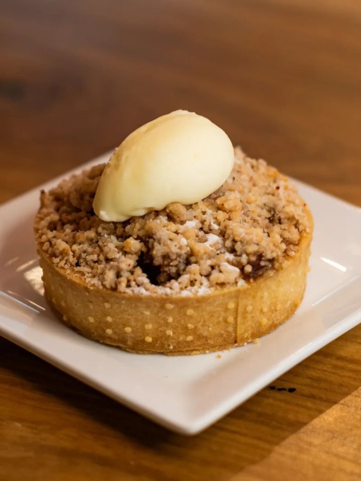 Golden apple crumble in a baking dish with a spoonful removed and a jug of custard beside it