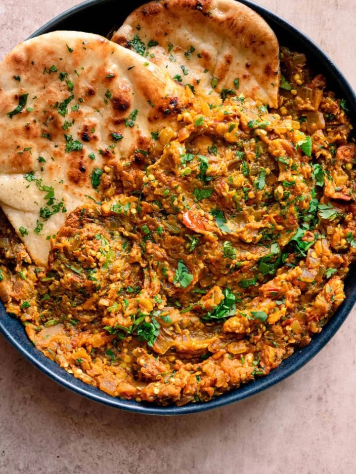 A pan of smoky Baingan Bharta garnished with coriander and ginger, served with roti and yogurt