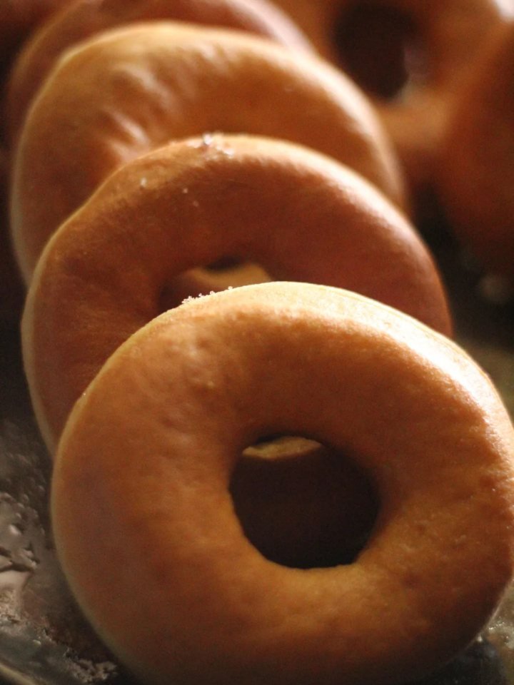 Glazed baked doughnuts with sprinkles cooling on a wire rack beside a cup of tea