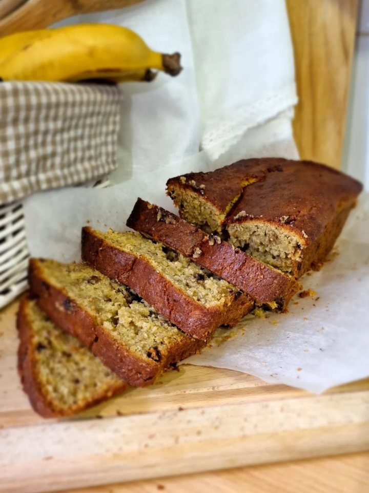 Sliced golden banana bread loaf with walnuts and butter on a wooden board