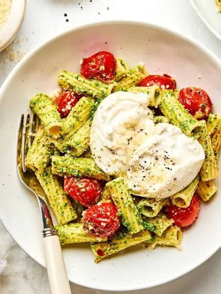 Bowl of spaghetti tossed in green basil pesto with blistered cherry tomatoes and grated Parmesan