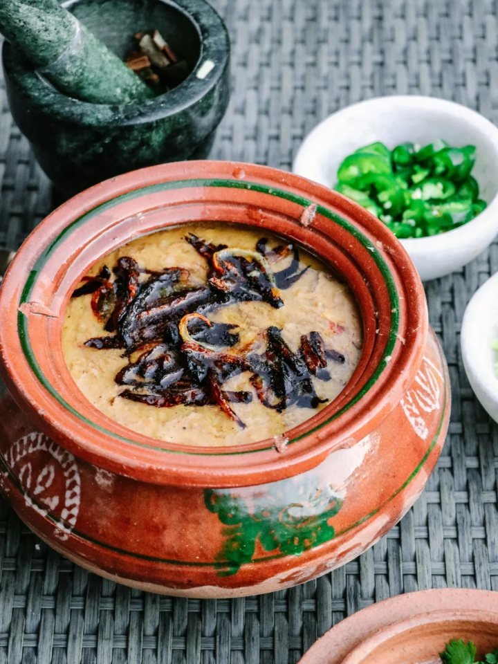 Bowl of beef haleem topped with fried onions, ginger, green chillies, fresh herbs and a lemon wedge