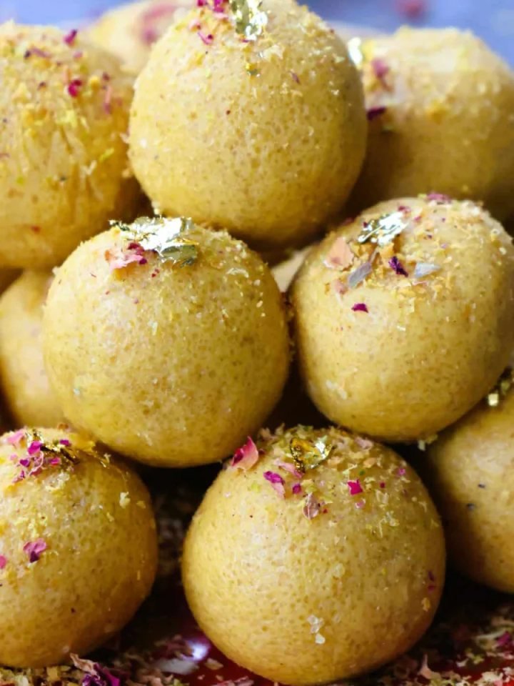 Golden besan ladoos topped with pistachio slivers on a brass plate