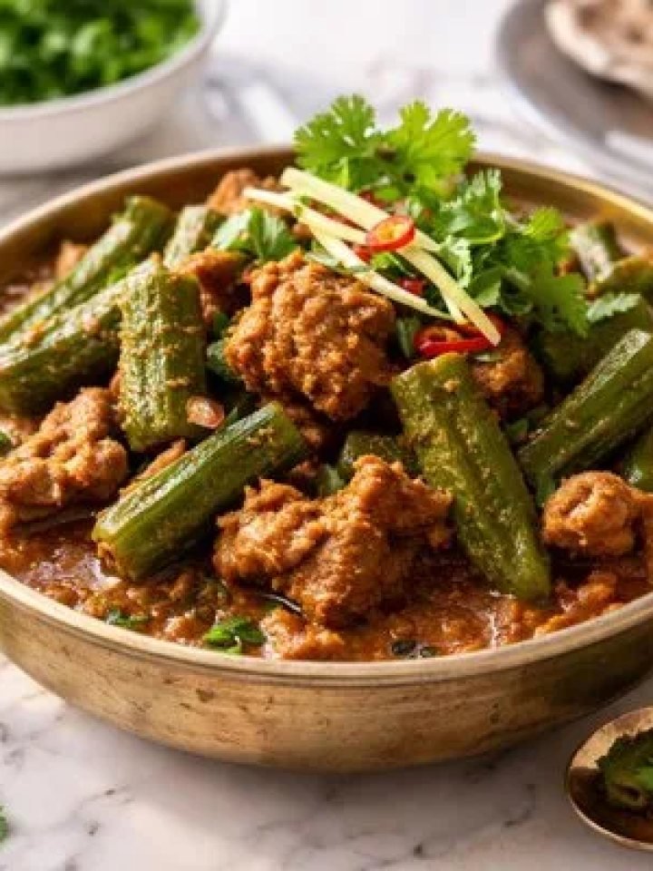 A pot of bhindi gosht with mutton pieces and green okra in a thick red-brown gravy, served with roti