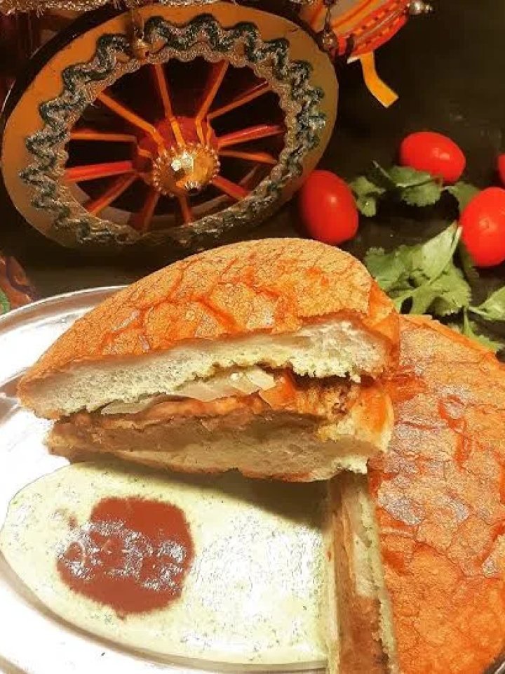 Bun kabab with a golden egg-coated beef patty, onion, tomato and green chutney in a toasted bun on a wooden board
