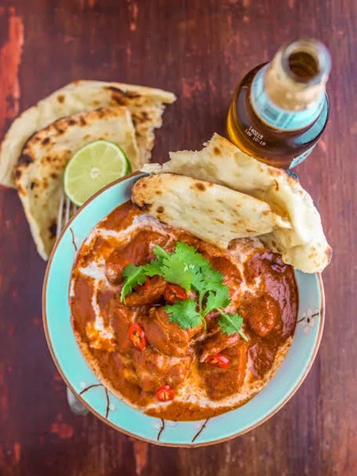 Bowl of creamy butter chicken with cream swirl and fresh coriander, served with naan and rice