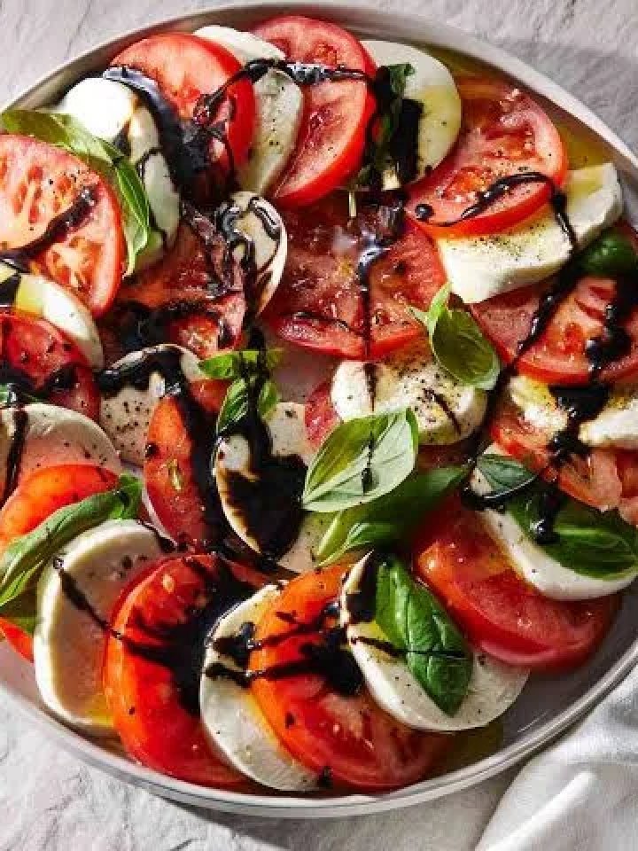 Caprese salad of sliced tomatoes, mozzarella and basil on a white platter with balsamic glaze