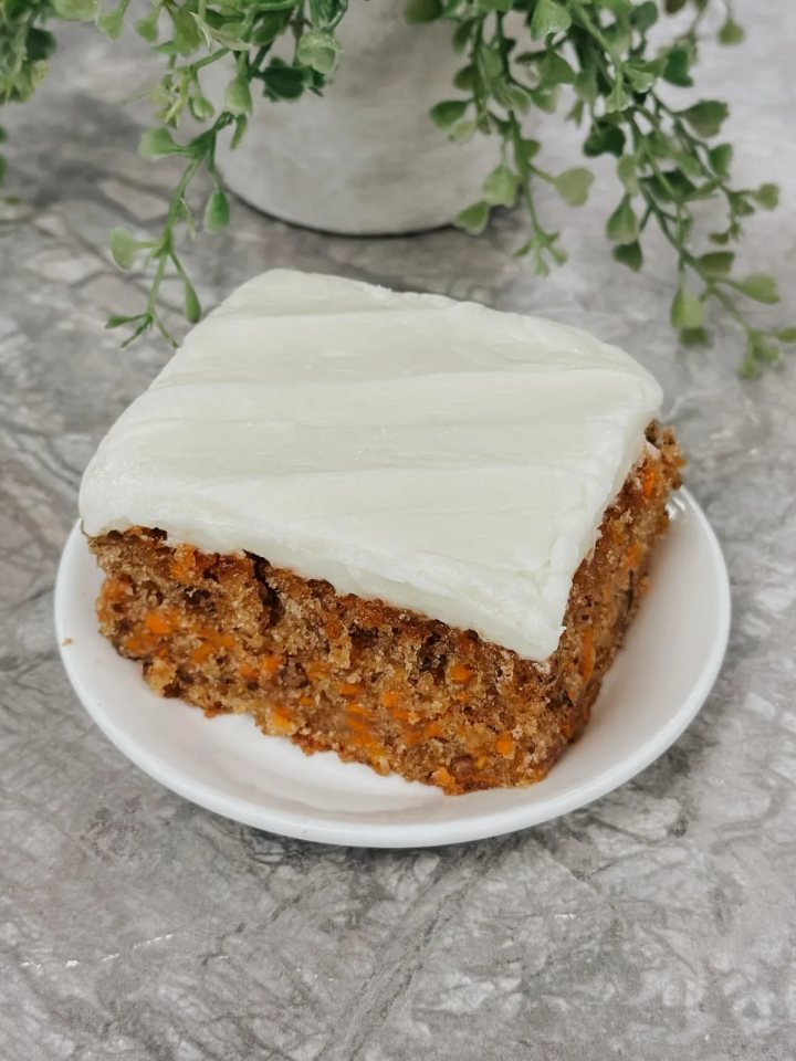 Sliced two-layer carrot cake with cream cheese frosting and chopped walnuts on a cake stand