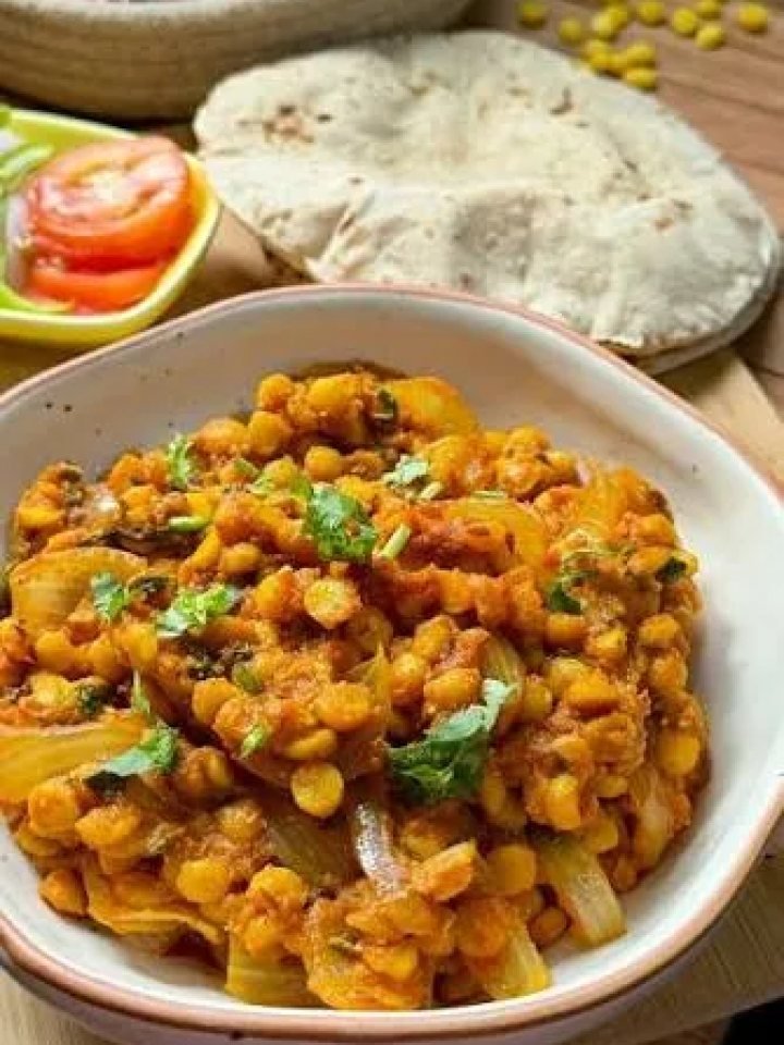 Bowl of golden chana daal topped with garlic tarka, chillies and fresh coriander, served with rice and roti