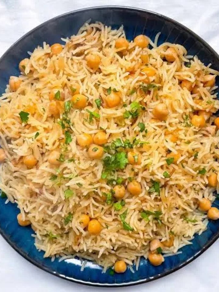 A dish of chana pulao with basmati rice, chickpeas, fried onions and fresh herbs, served with raita and lemon.
