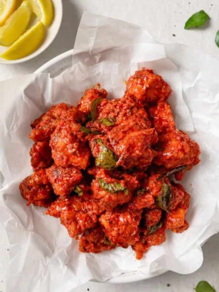 A plate of crispy red Chicken 65 with curry leaves, green chillies, onion rings and lemon wedges