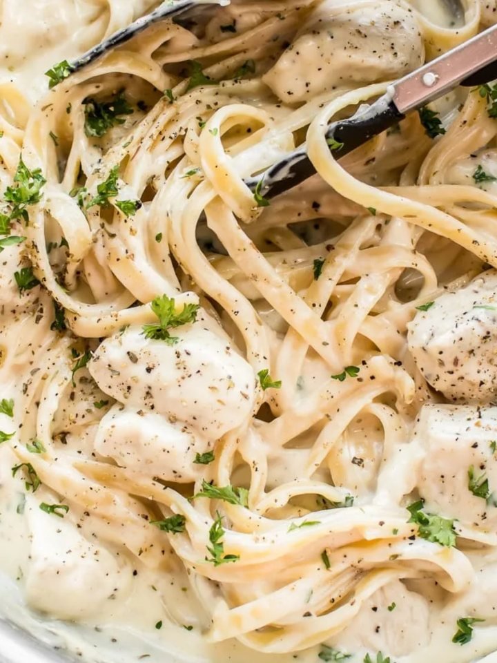A bowl of fettuccine Alfredo topped with sliced seared chicken, parsley and grated Parmesan