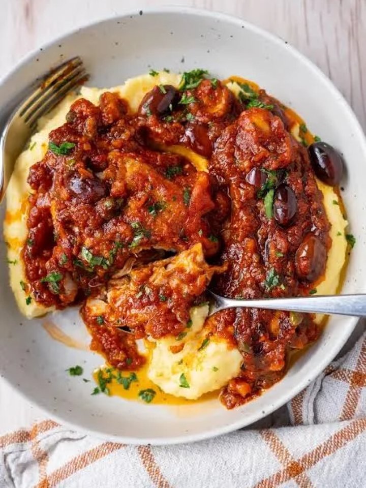 Skillet of chicken cacciatore with browned chicken pieces in tomato sauce with peppers, mushrooms, olives and parsley