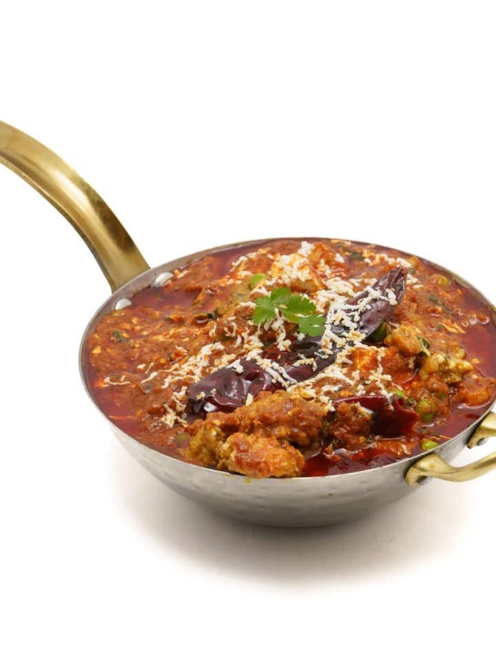 A pan of dark, peppery chicken Chettinad curry topped with curry leaves and fresh coriander, served with rice and paratha