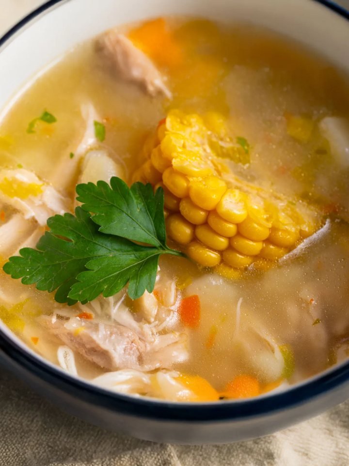 Bowl of golden chicken corn soup with shredded chicken, corn kernels, egg ribbons and spring onion