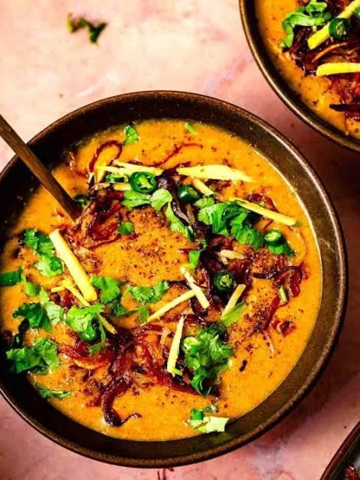 Bowl of Pakistani chicken haleem topped with fried onions, ginger, green chillies, herbs and lemon wedges